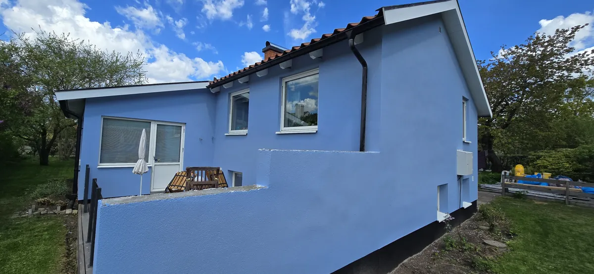 Blue-painted rendered walls with white windows on a detached house in Ängelholm.