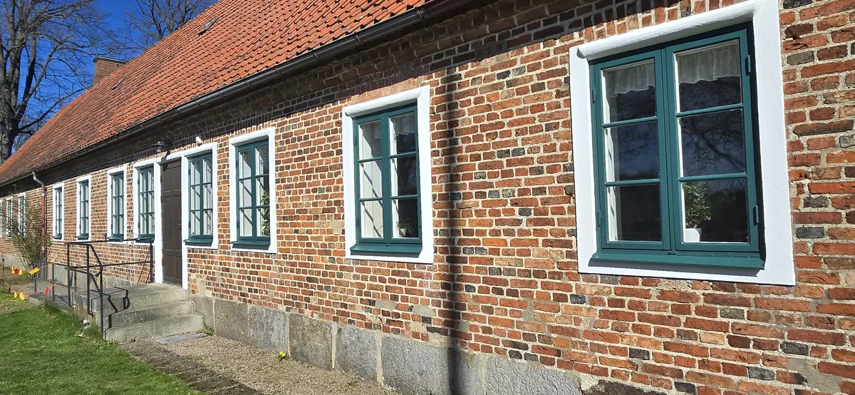 Gröna träfönster med vita omfattningar i en tegelfasad vid Kvidinge kyrka.