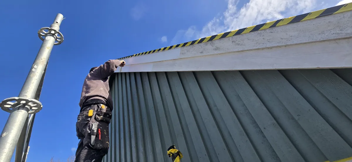 Painter working on a white bargeboard above green timber cladding in Löddeköpinge.