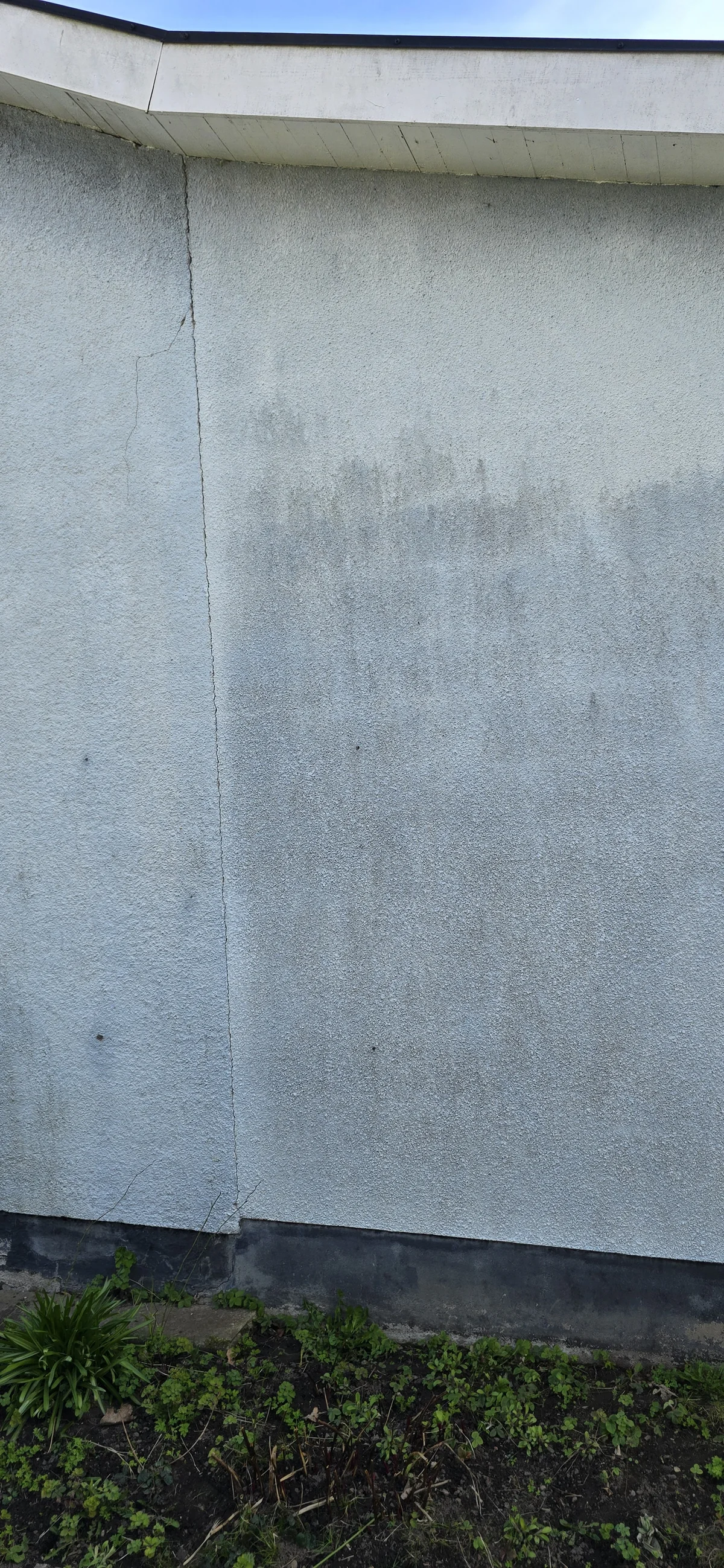 Light-coloured rendered façade with a visible crack below the eaves.