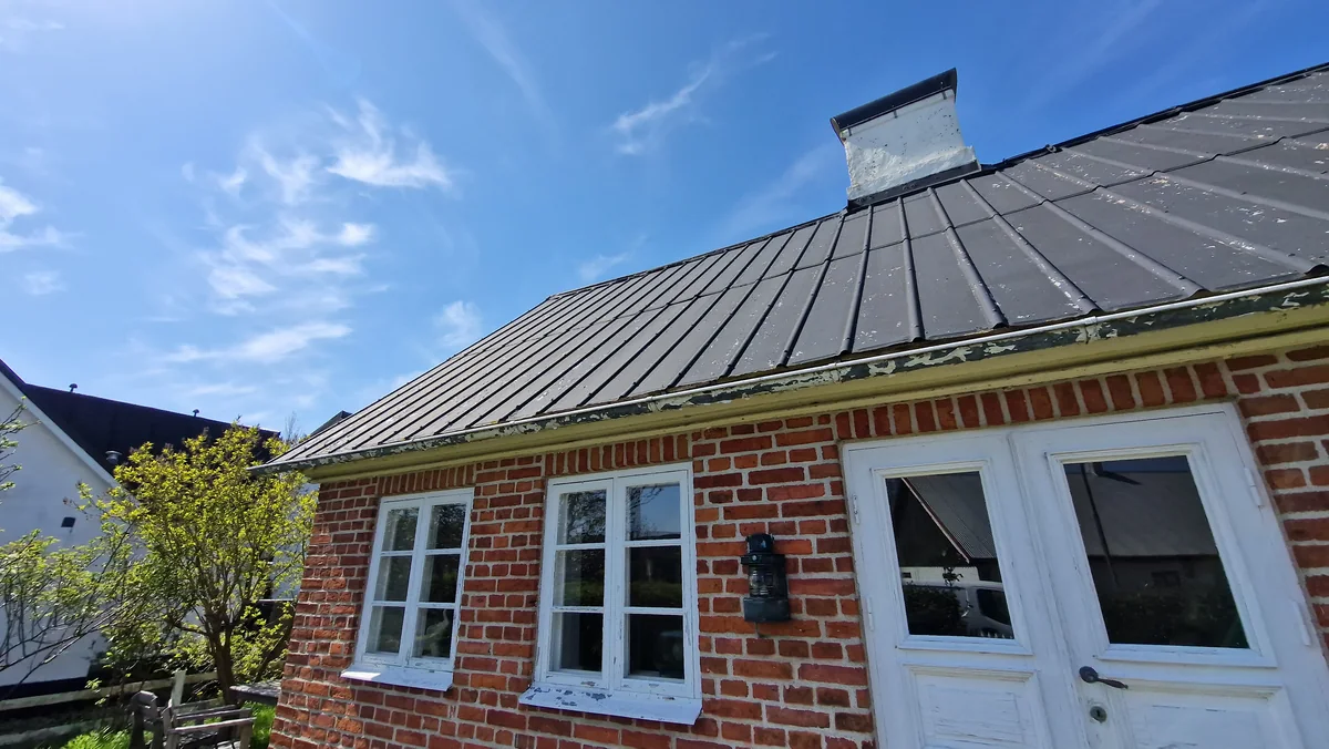 Standing-seam metal roof with a chimney above a brick house.