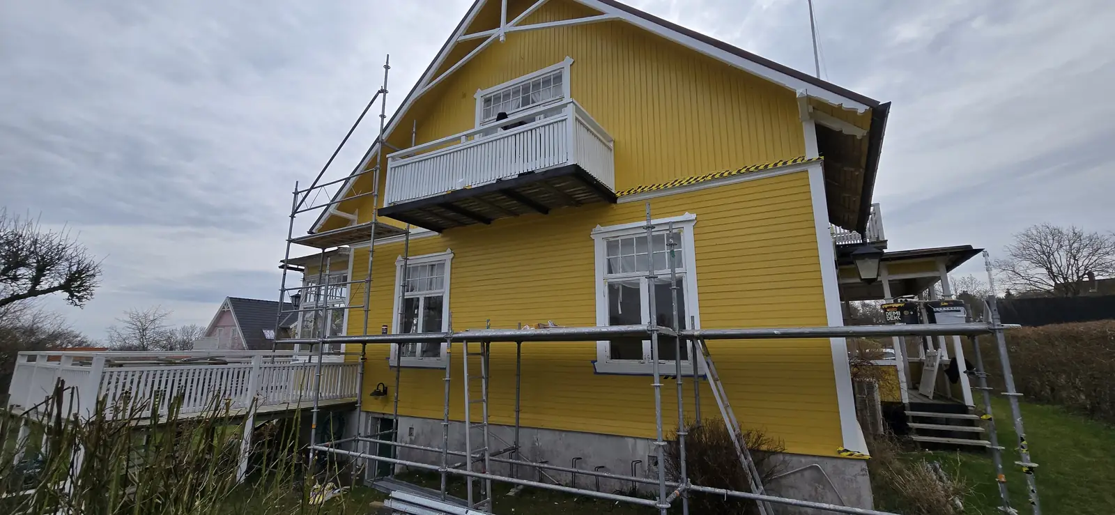 Yellow timber façade with white windows and scaffolding in front of the house.