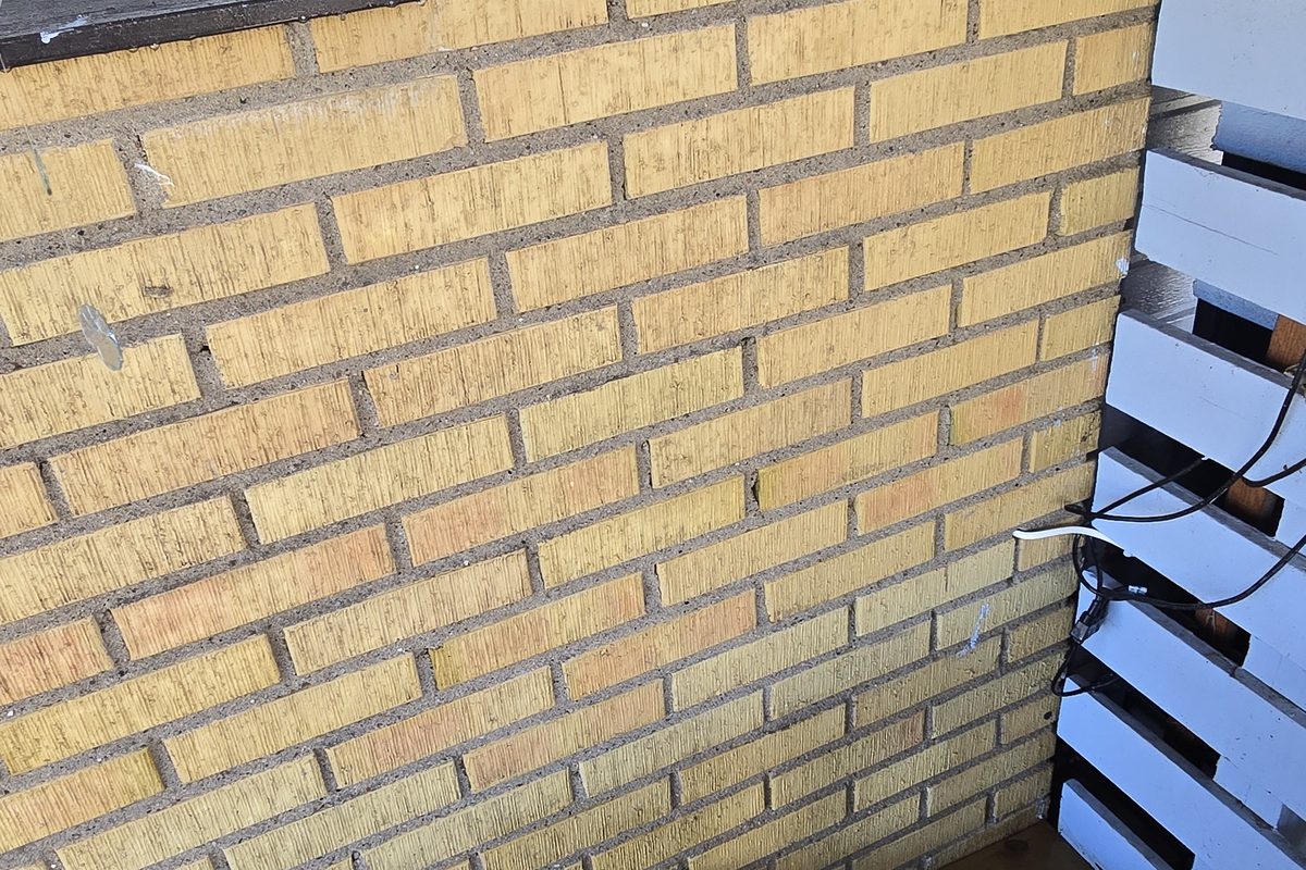 Detalj av det omålade gula teglet i Åkarp sett underifrån, med träunderpanel och kabelgenomföringar i fasaden