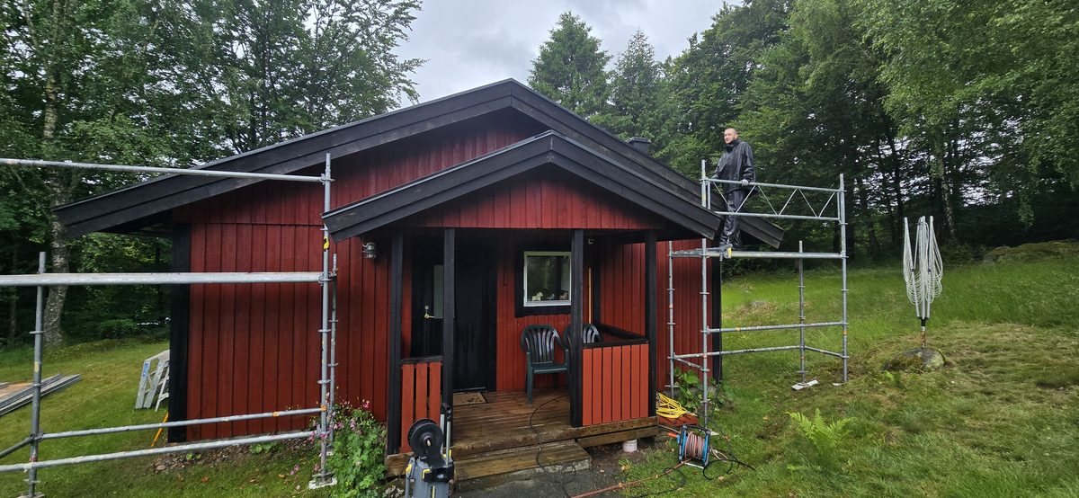 Rödmålat trähus i Lycke med byggnadsställning uppställd längs två fasader och en målare på ställningen