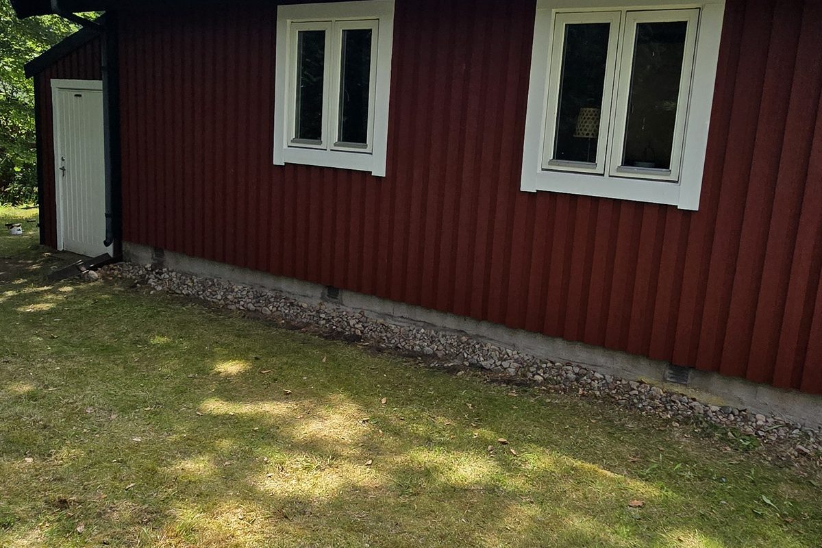 Närbild på den rödmålade träpanelen i Lycke med två vita ventiler infällda i fasaden