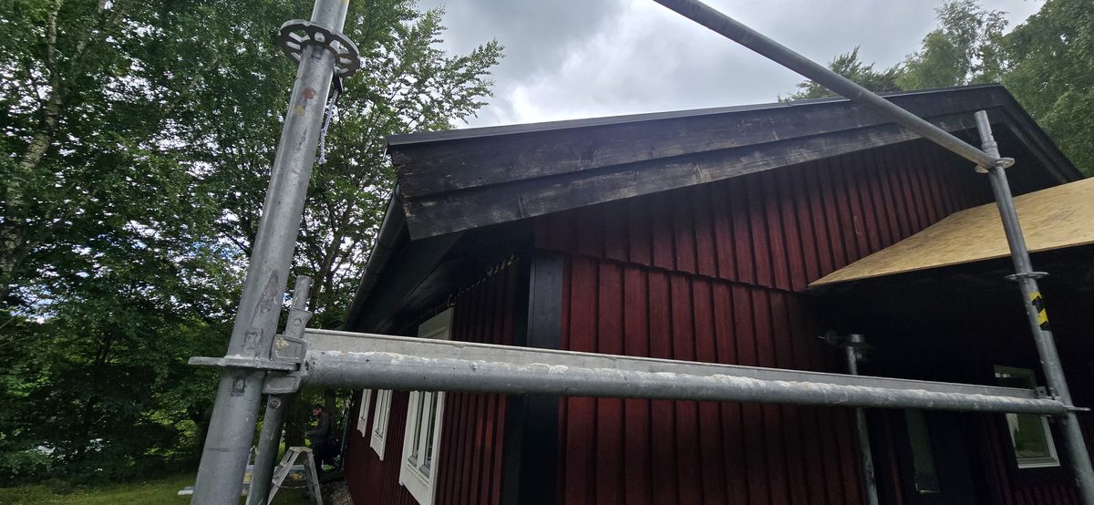 Byggnadsställning rest mot gaveln på en rödmålad träbyggnad i Lycke inför ommålning av fasaden