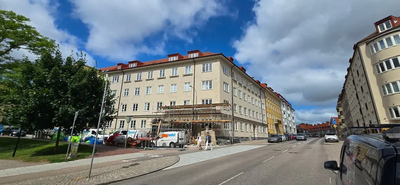 Ljus putsfasad på flerbostadshus i Stattena, Helsingborg, med ställning längs bottenvåningen.