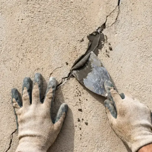 Hand spacklar en spricka i en putsfasad