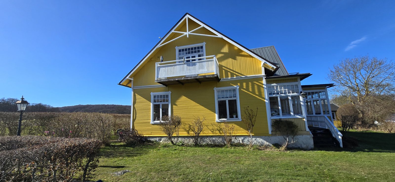 Gult trähus i Arild i helbild med glasveranda och vitmålade snickerier