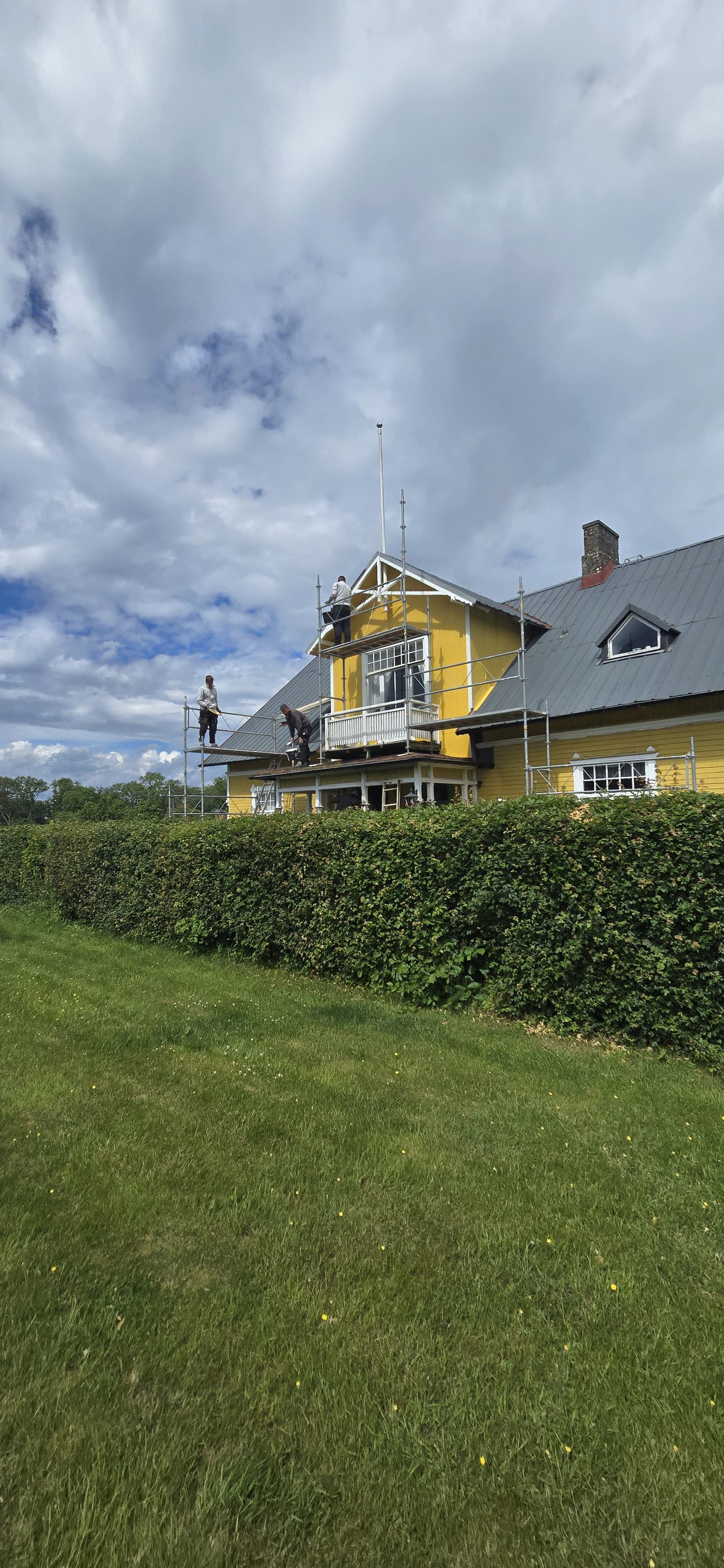 Ställning mot gaveln på trähuset i Arild med tre målare i arbete på balkong och vindskivor