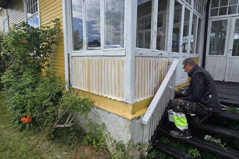 Målare från NLL Måleri stryker den vita glasverandan på ett gult trähus i Arild på Kullahalvön
